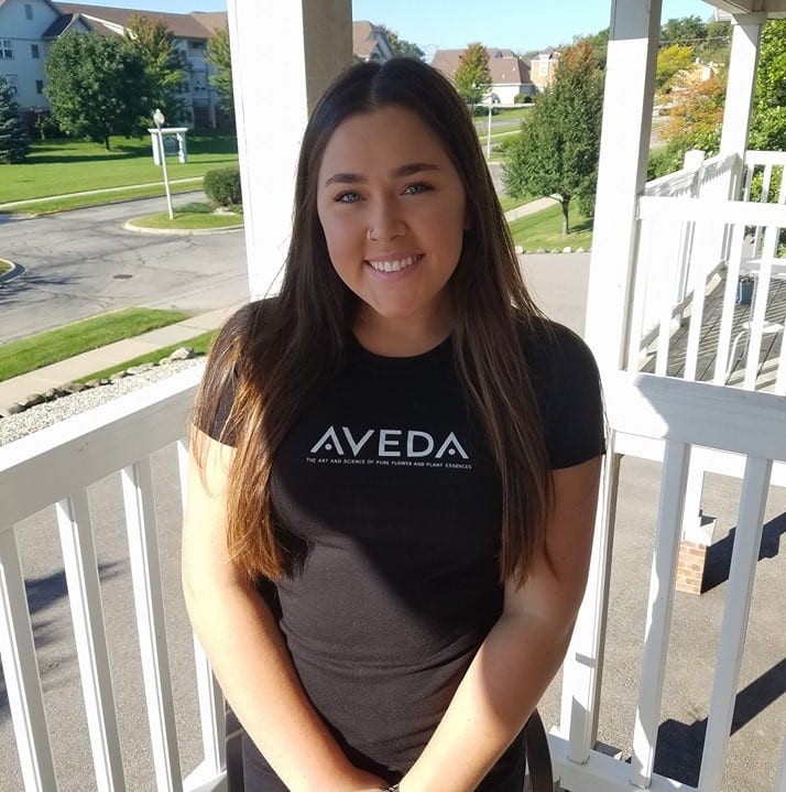 young woman in black Aveda tshirt on a white porch outside