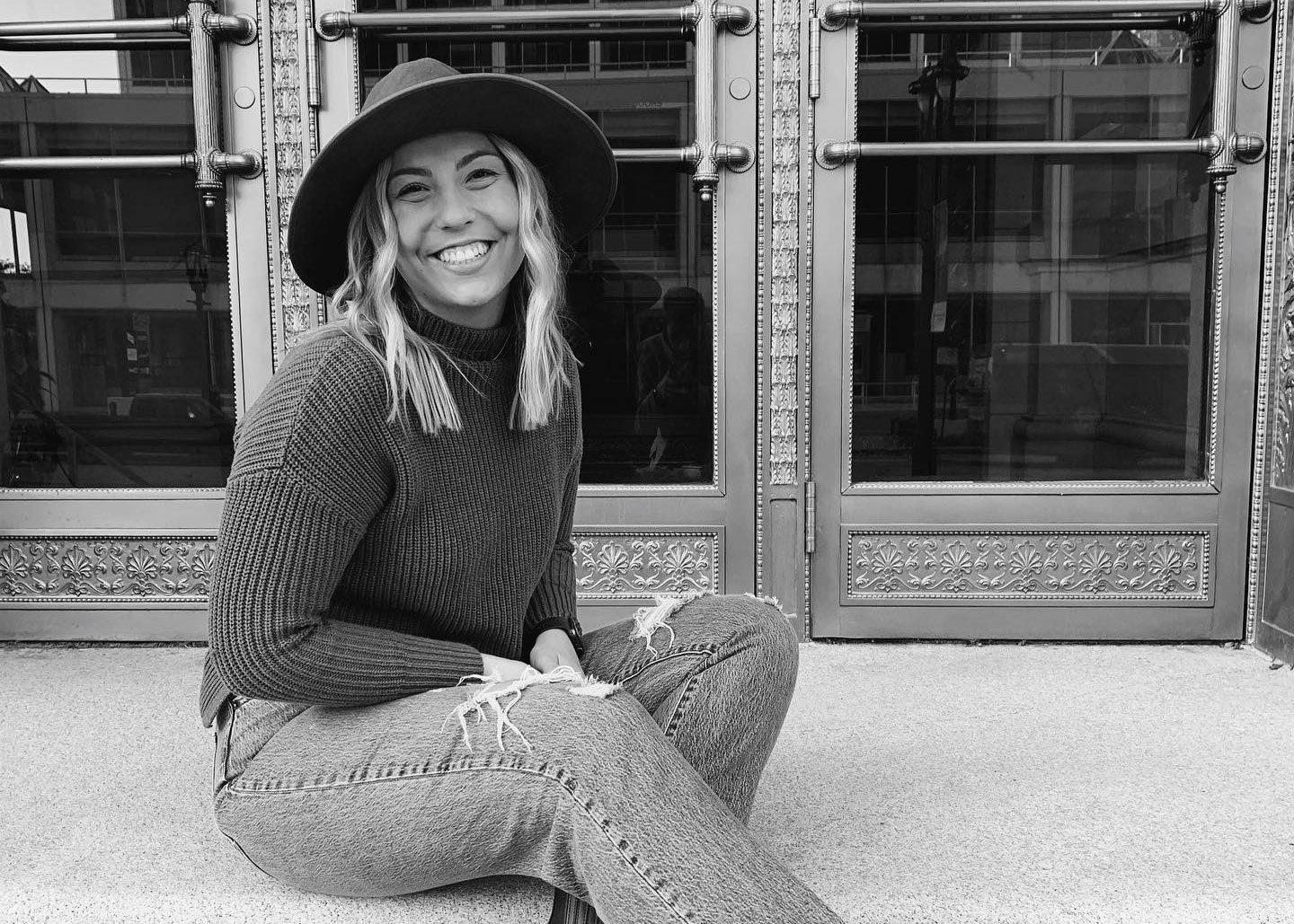**A woman in a hat and jeans sitting on steps.**
