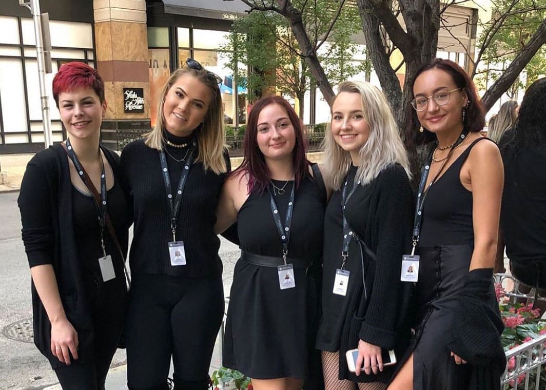 **Five women in matching black attire, striking a pose for a group picture.**