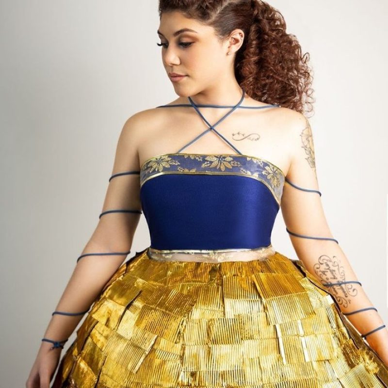 **A woman in a gold and blue dress, made of recycled materials, standing gracefully.**