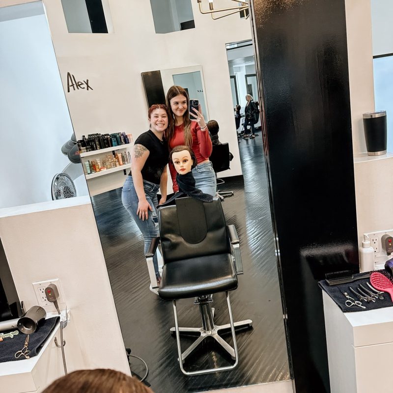 A cosmetology Mannequin head in a salon chair, surrounded by students in the Vidal Sassoon salon for advanced training.